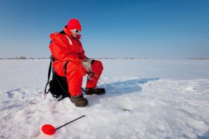 man in red survival suit ice fishing on lake winnipeg