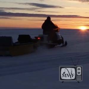 man driving a snowmobile on lake winnipeg towards the setting sun