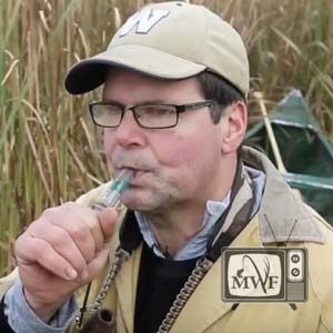 man blowing a duck call in the marsh